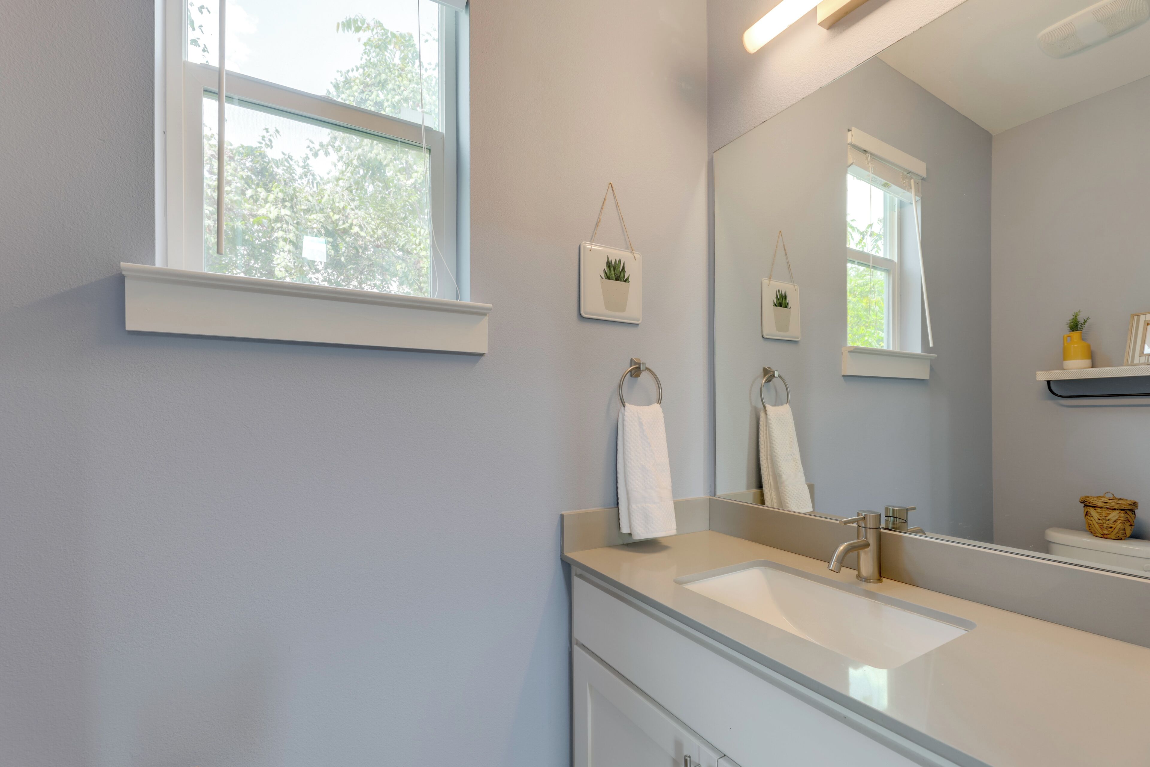 A bathroom with a large mirror, a sink, and two windows.