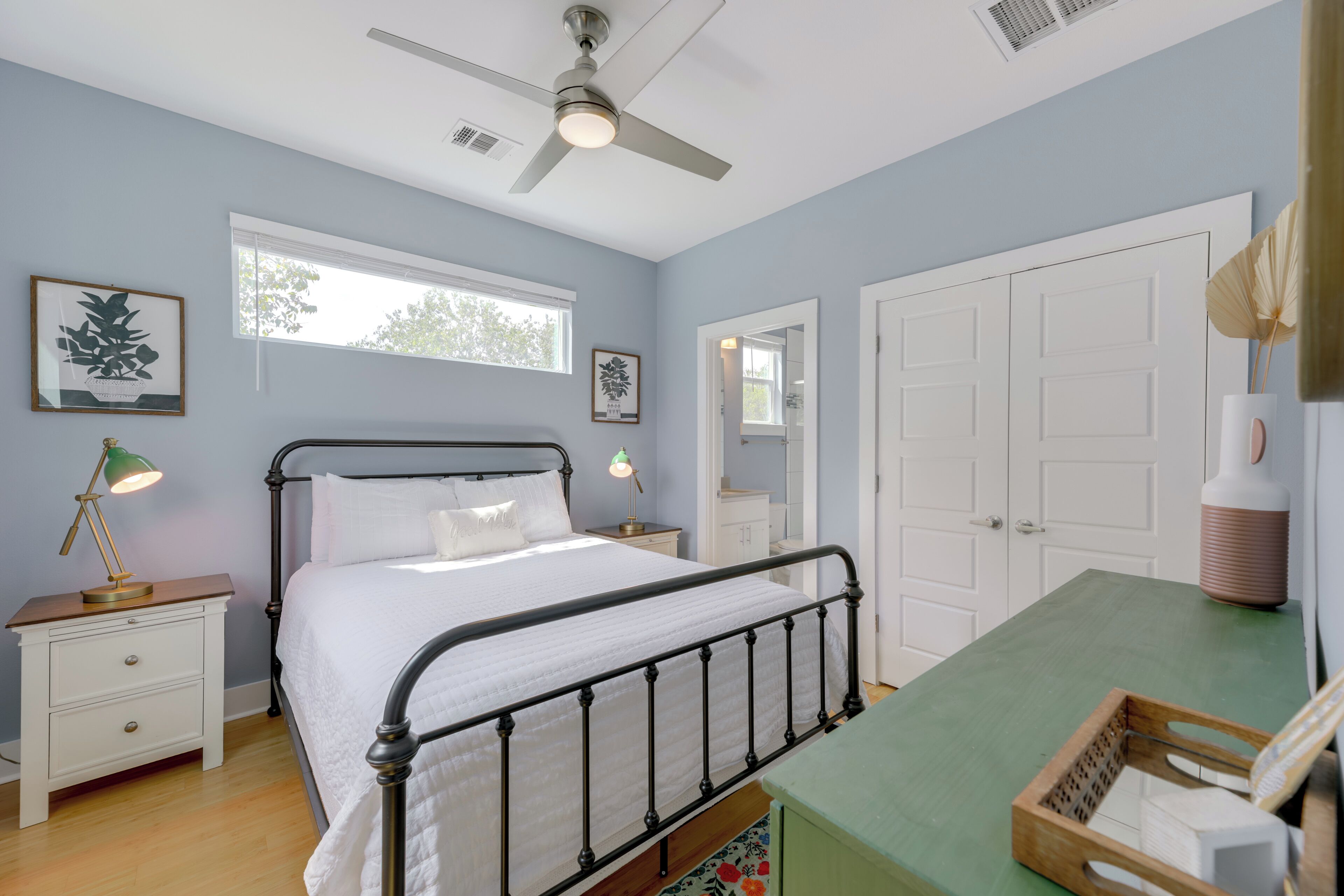 A bedroom with a bed, bedside tables, a ceiling fan, a window, and a door.
