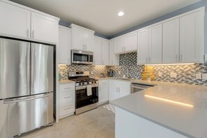 Una cocina moderna con armarios blancos, electrodomésticos de acero inoxidable y salpicadero de azulejos.