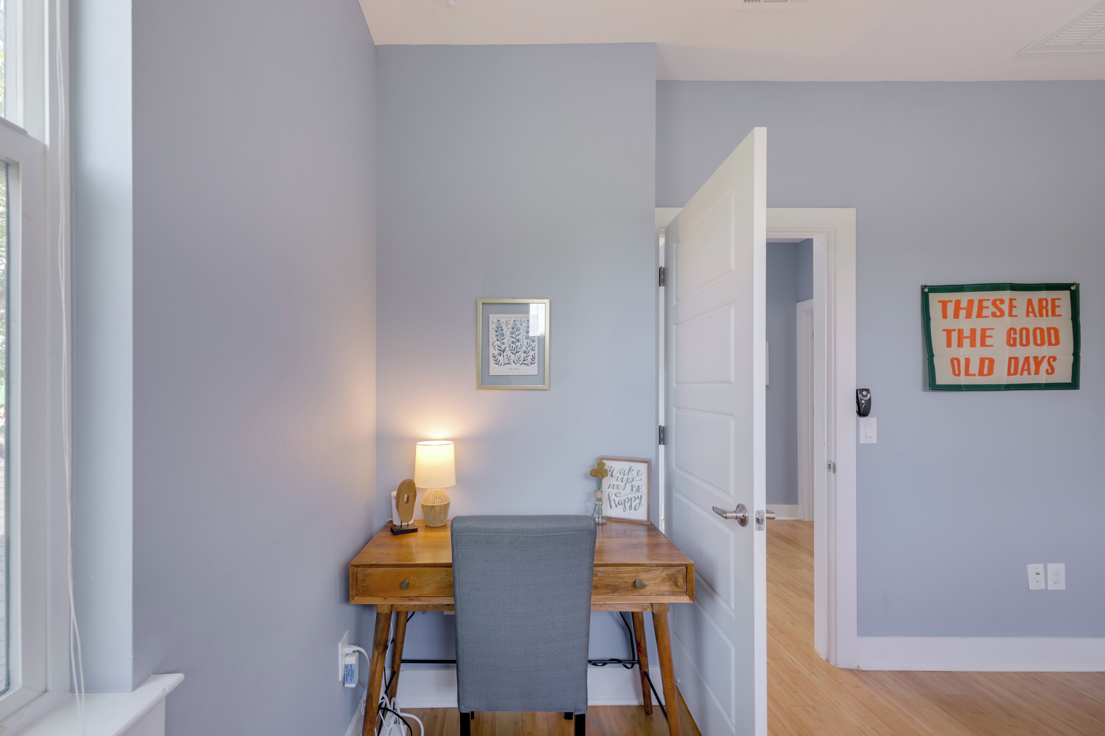 A room with a wooden desk, a lamp, a framed picture, and a motivational quote on the wall.