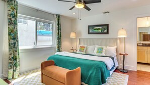 A bedroom with a bed, a bench, a ceiling fan, a window, and a nightstand with a lamp. - Cowboy Pool & Balcony: Home 1 Mi to Dtwn Austin! (Austin)