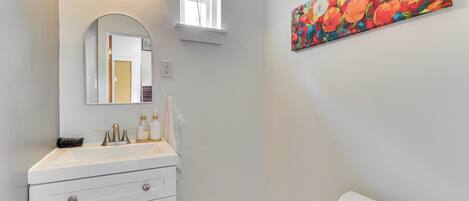 A bathroom with a white sink, a mirror, a painting of flowers, and a toilet.