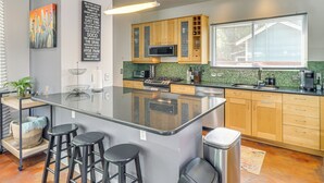 A modern kitchen with a central island, bar stools, wooden cabinets, a microwave, and a large window. - Cowboy Pool & Balcony: Home 1 Mi to Dtwn Austin! (Austin)