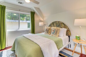 Un dormitorio ordenado con cama, mesita de noche, lámpara y ventana con cortinas.