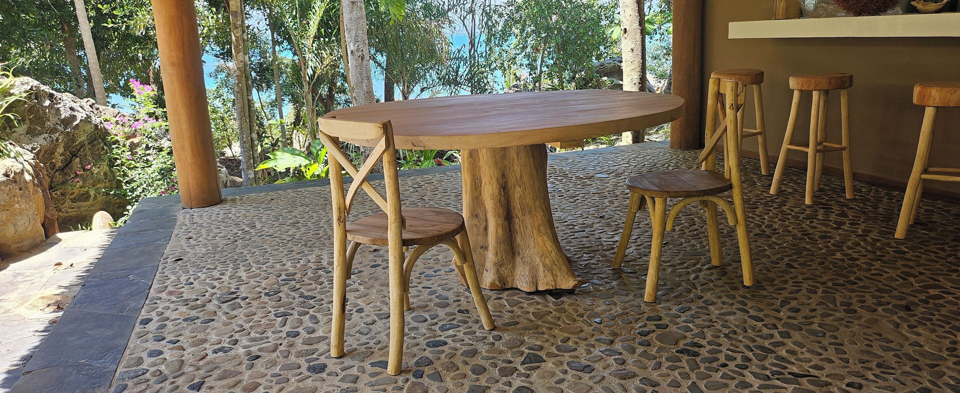 A wooden table with a natural wood base, surrounded by matching wooden stools, set on a pebble-patterned floor.