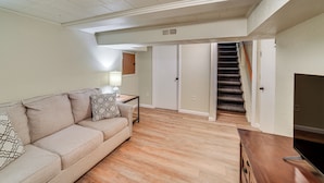 Un salon avec un canapé beige, une table basse en bois et un meuble pour la télévision. Un escalier mène à l’étage supérieur.