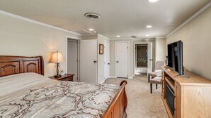 Une chambre à coucher comprenant un grand lit, une commode, un téléviseur et une porte donnant sur une salle de bain.