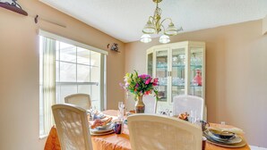 A dining area with a table set for four, chairs, a vase with flowers, and a cabinet with glassware. - Spacious Palm Bay Stay! Family Home Near Beaches (Palm Bay)
