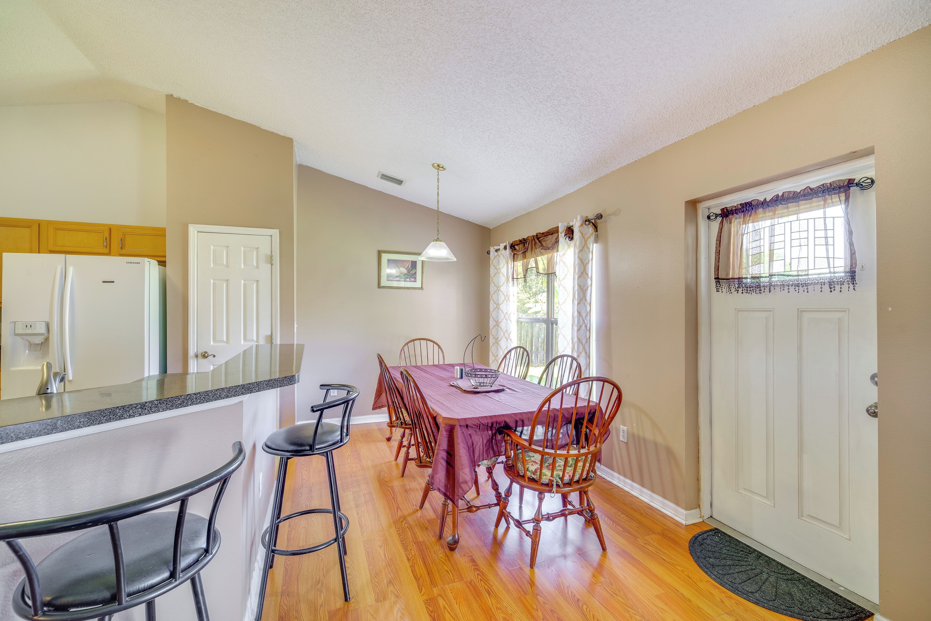A dining area with a wooden table, six chairs, a refrigerator, and a kitchen counter.