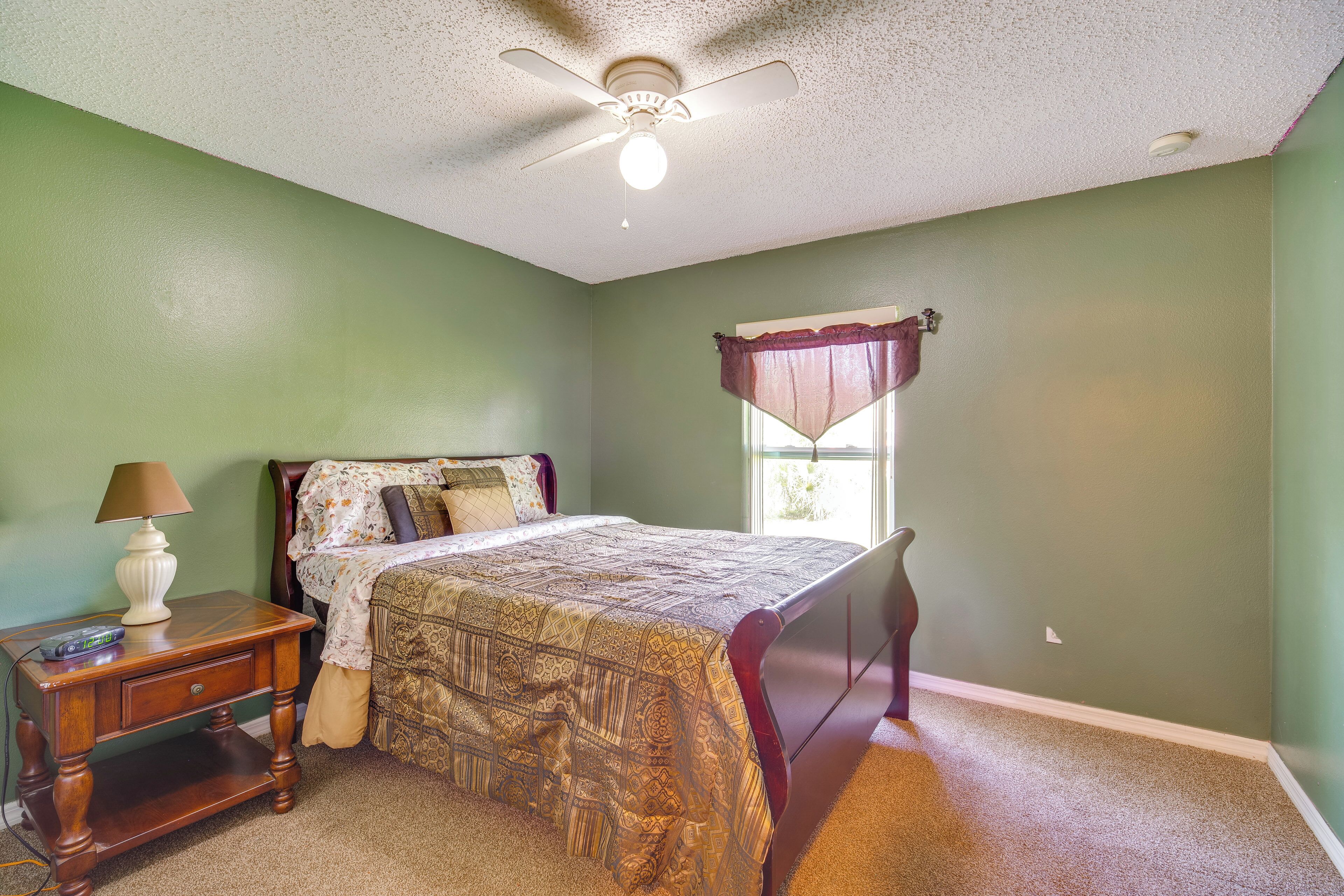 A bedroom with a bed, nightstand, lamp, ceiling fan, and window with curtains.