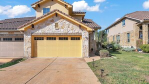 A two-story house with a yellow garage door, stone facade, and a tiled roof. - 5 Mi to Lake Travis: Pet-friendly Home w/ Yard! (Lakeway)
