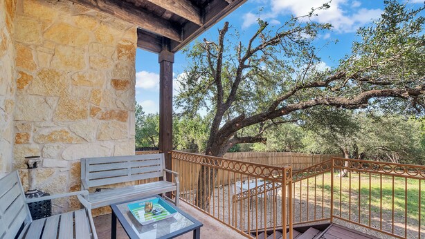 A covered patio with stone walls, a wooden bench, a table with a menu, and a view of trees and grass. - 5 Mi to Lake Travis: Pet-friendly Home w/ Yard! (Lakeway)