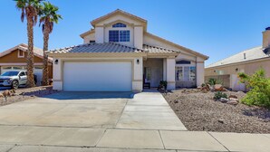 A two-story house with a garage, a driveway, and a landscaped front yard with palm trees and rocks. - Pool, Games & Patio Bar! Epic Bullhead City Oasis (Bullhead City)