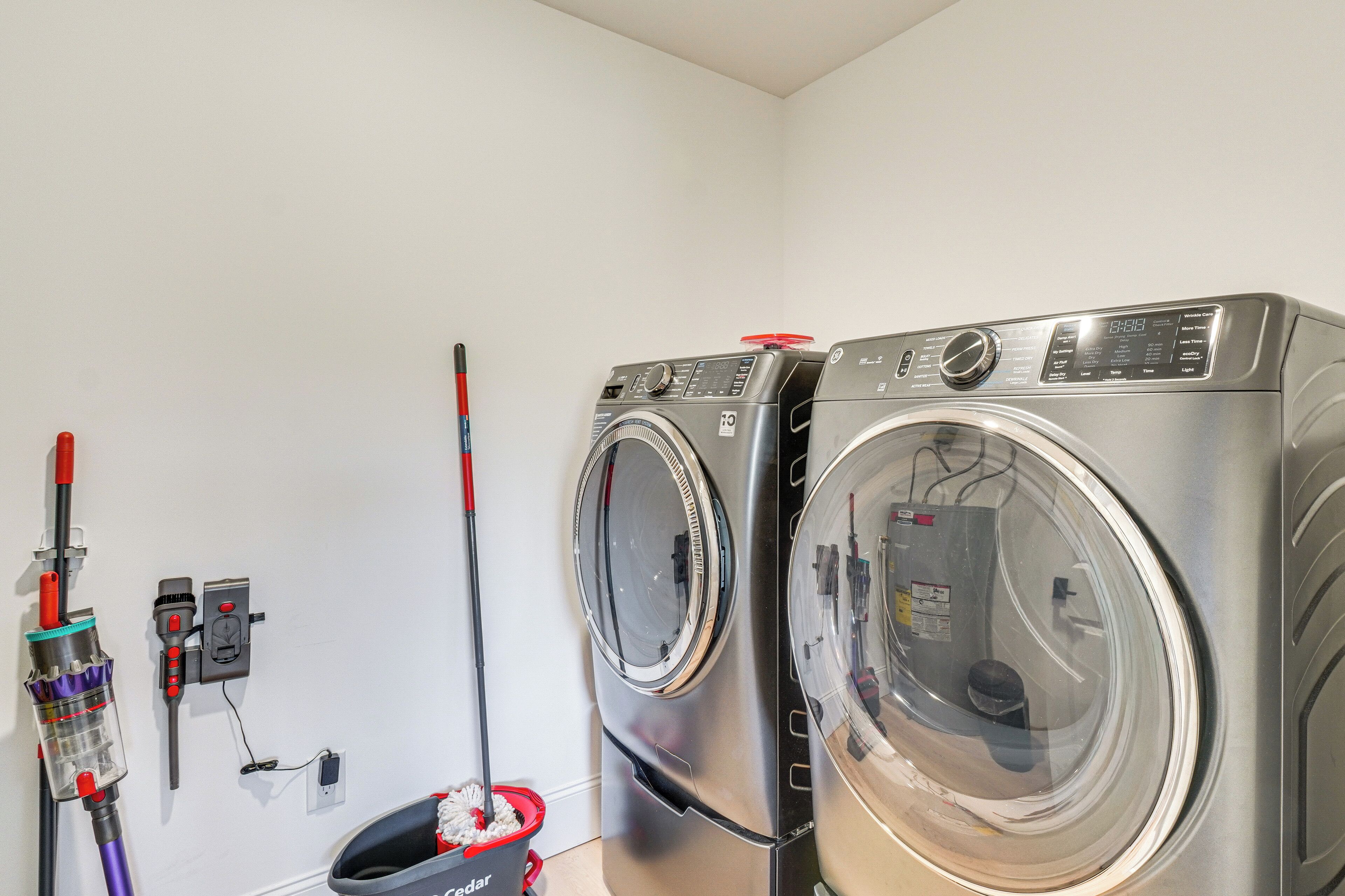 Un espace buanderie comprenant deux machines à laver à chargement frontal, un aspirateur et un balai.