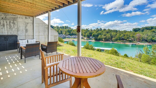 A covered outdoor area with a wooden table and chairs, a concrete wall, and a view of a lake and forest. - Private Boat Slip, Scenic Views: Norris Lake Condo (La Follette)