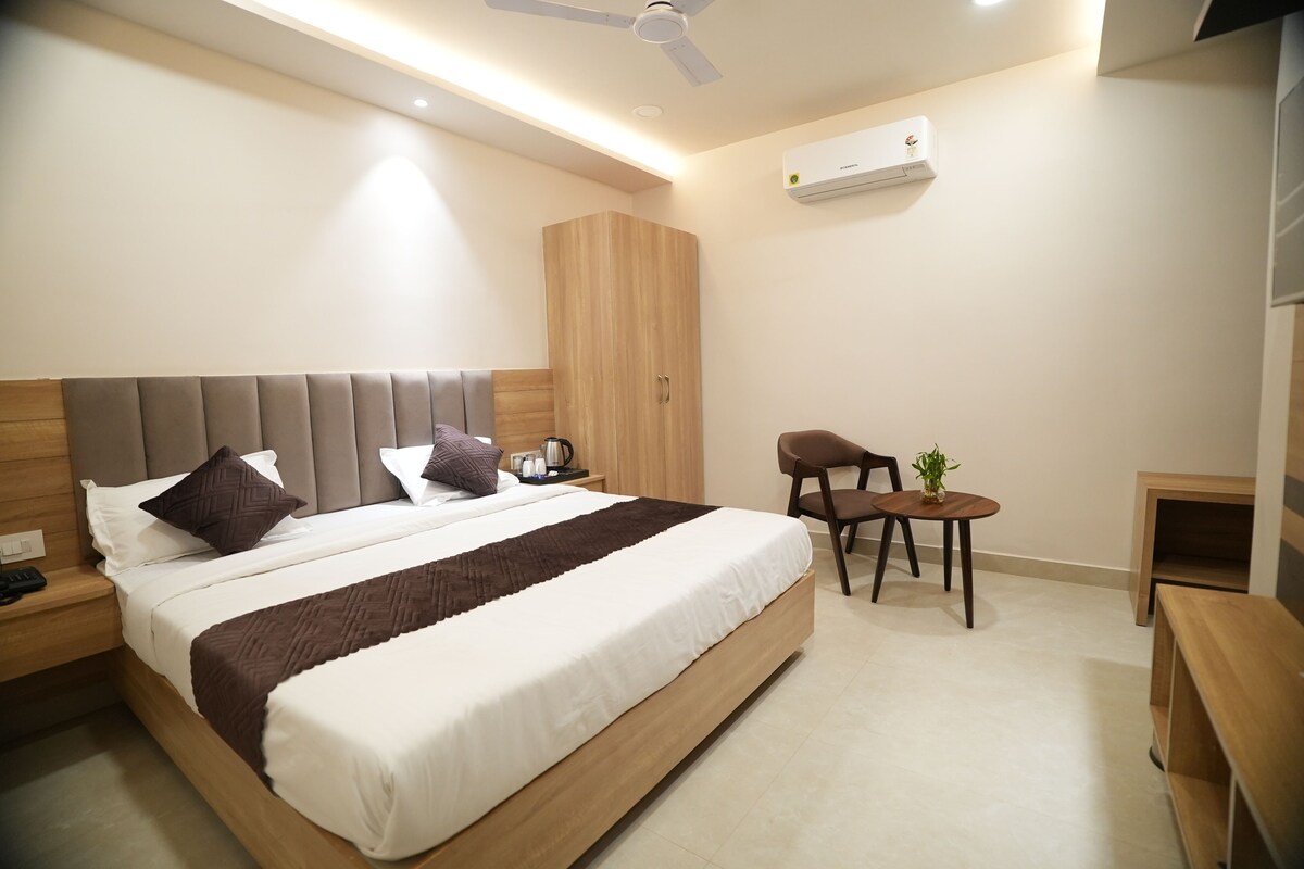 A modern hotel room with a large bed, a wooden wardrobe, a small table with a plant, and a ceiling fan.