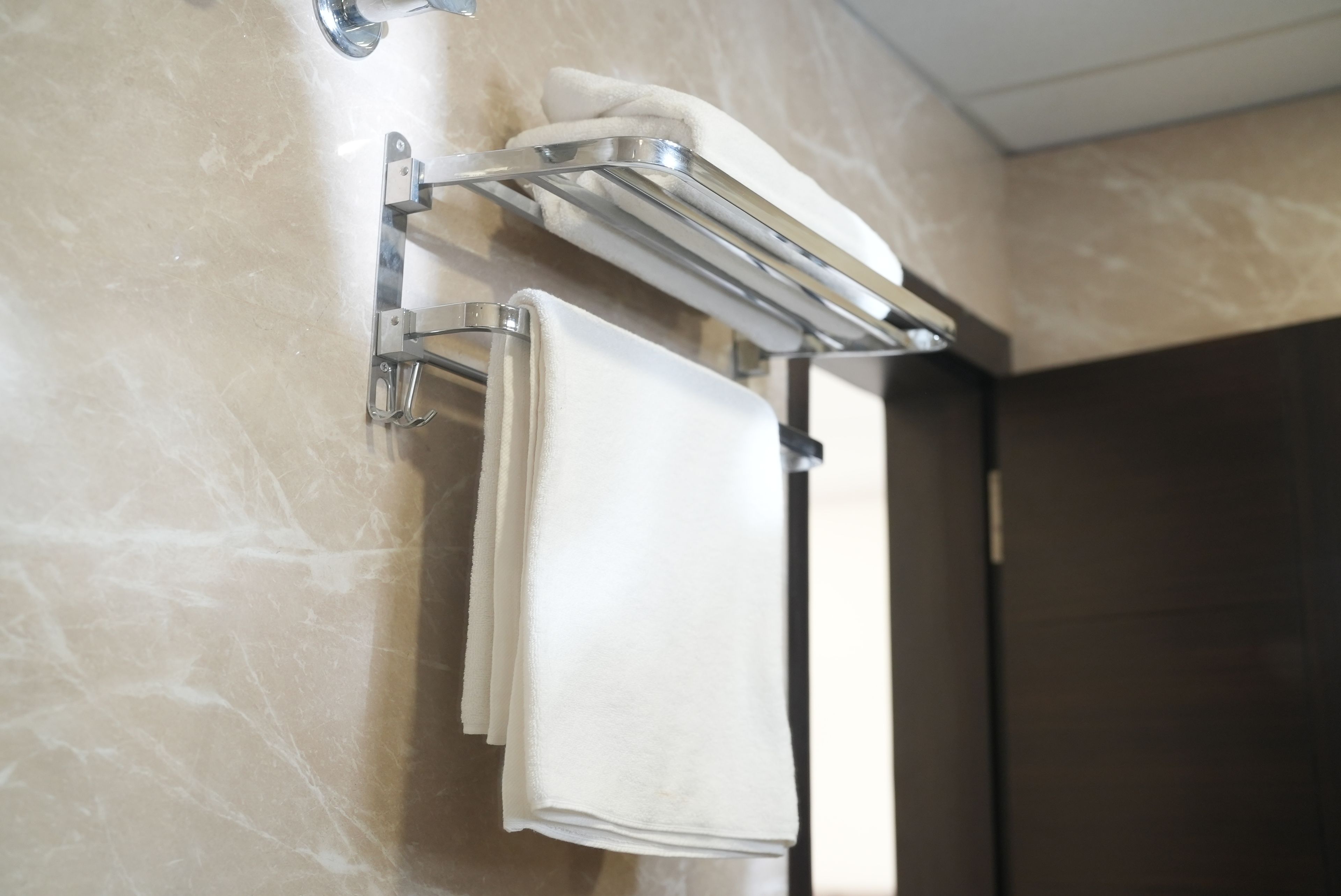 A bathroom with a towel rack holding two folded towels and a towel on a shelf.