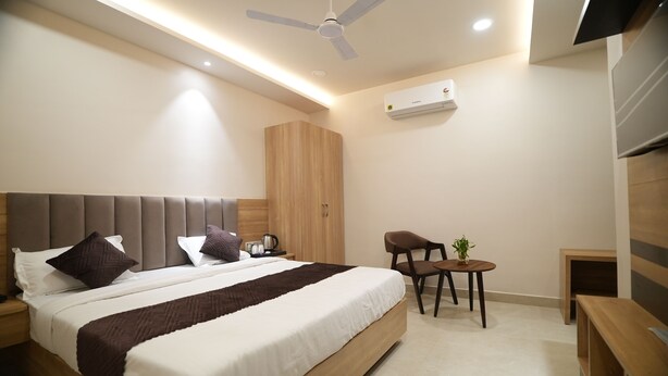 A modern bedroom with a large bed, bedside tables, a ceiling fan, an air conditioning unit, and a small seating area with a plant. - Pearl of Varanasi (Varanasi)