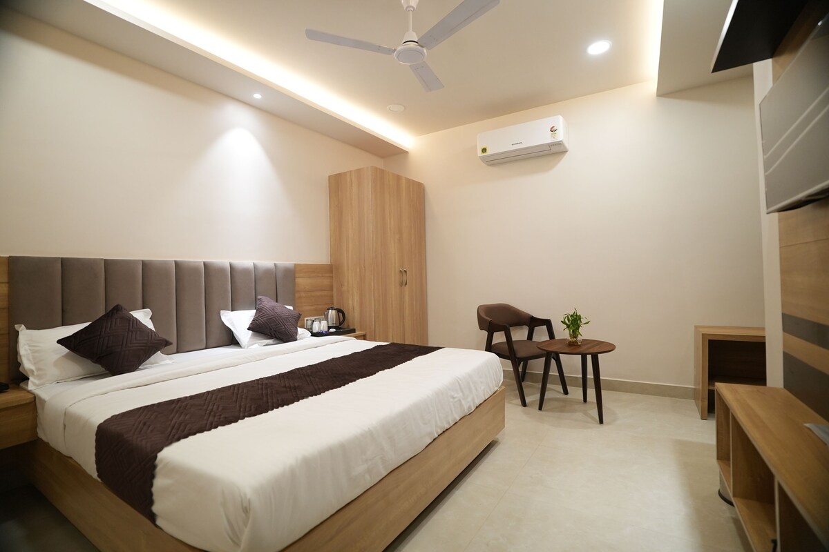 A modern bedroom with a large bed, bedside tables, a ceiling fan, an air conditioning unit, and a small seating area with a plant.