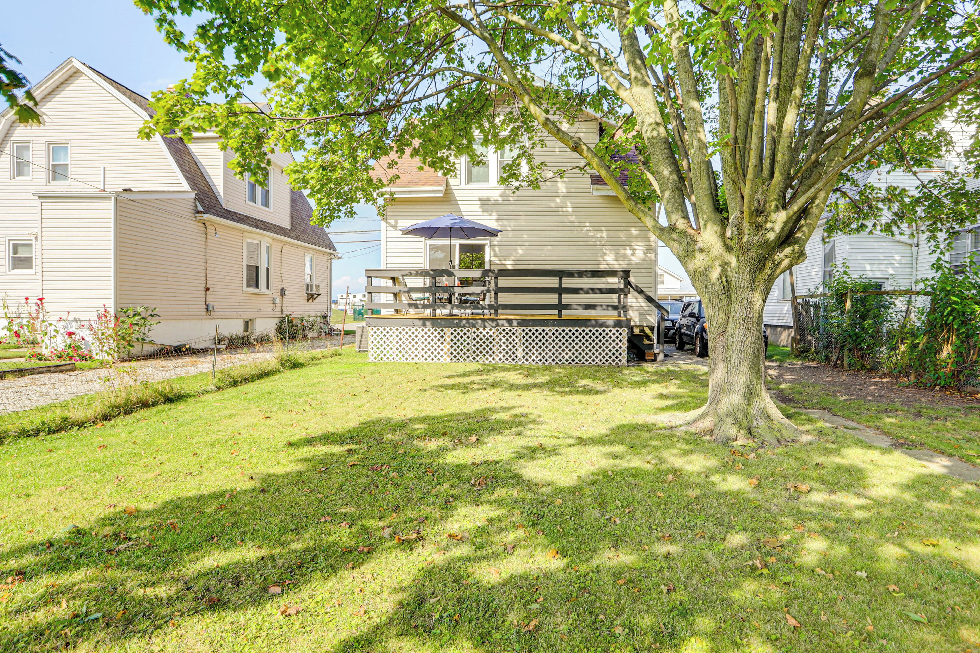 A residential property with a well-maintained lawn, a wooden deck, and a large tree providing shade.