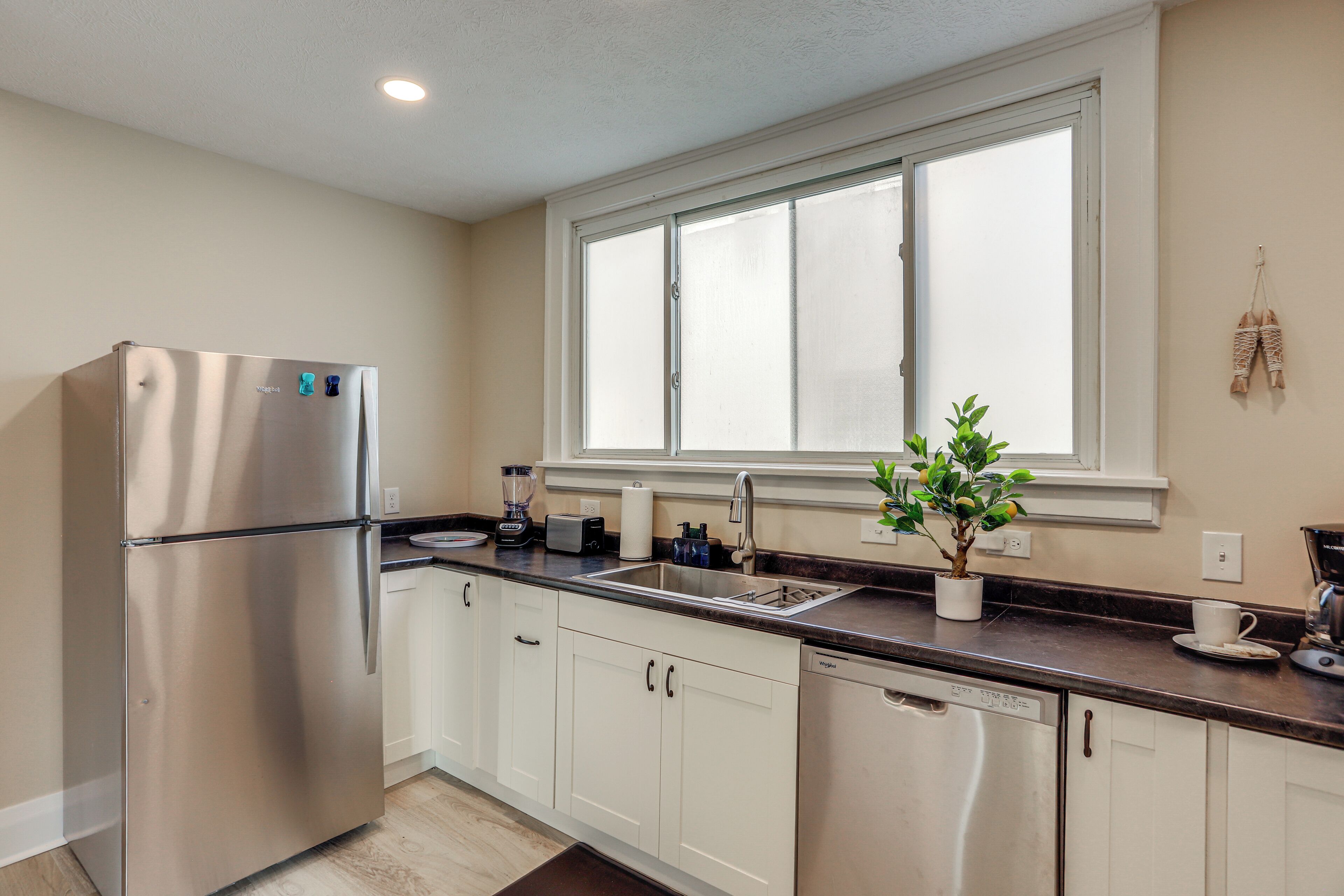A modern kitchen with a stainless steel refrigerator, a built-in dishwasher, a window above the sink, and a potted plant on the counter.