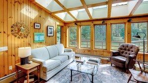 A cozy living room with a wooden interior, a sofa, a glass coffee table, and a leather armchair. - Secluded Family Getaway w/ On-site Creek in Hawley (Charlemont)