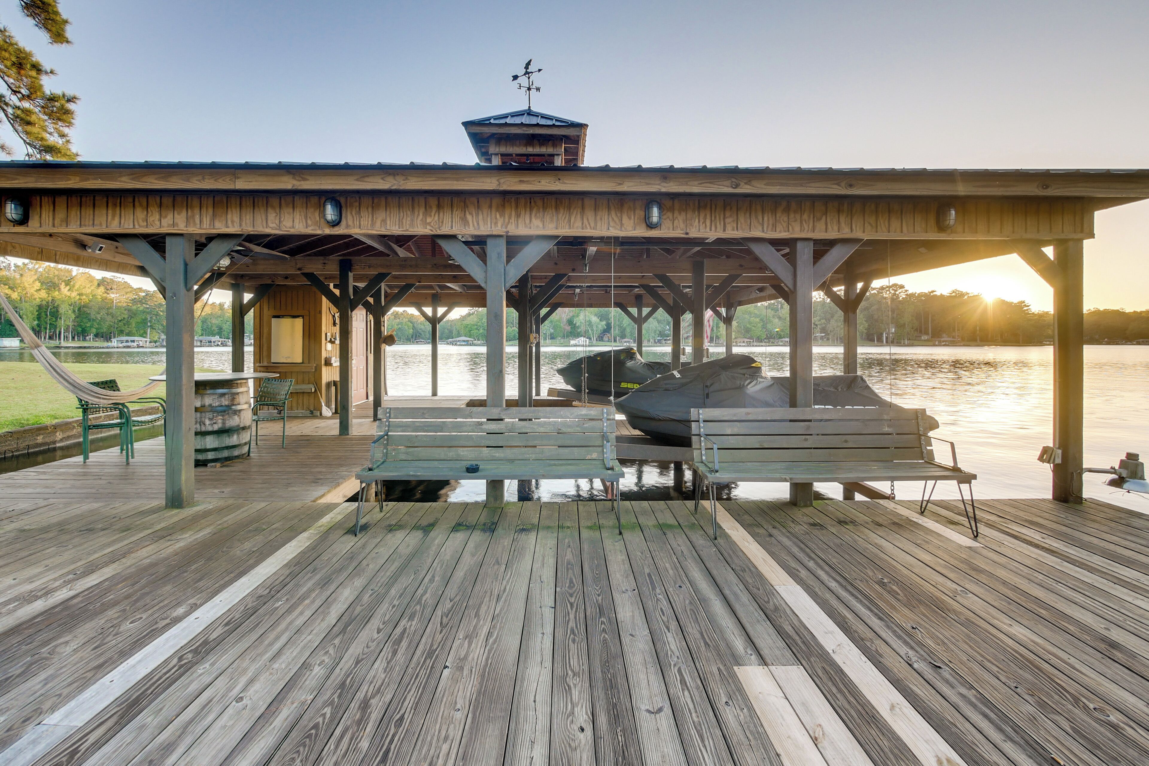 A wooden pier with benches and a covered area, overlooking a calm lake.