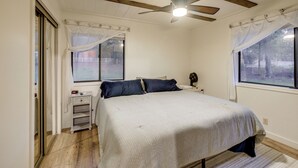 Una camera da letto con un letto, una ventola a soffitto, un comodino e una finestra con tende.