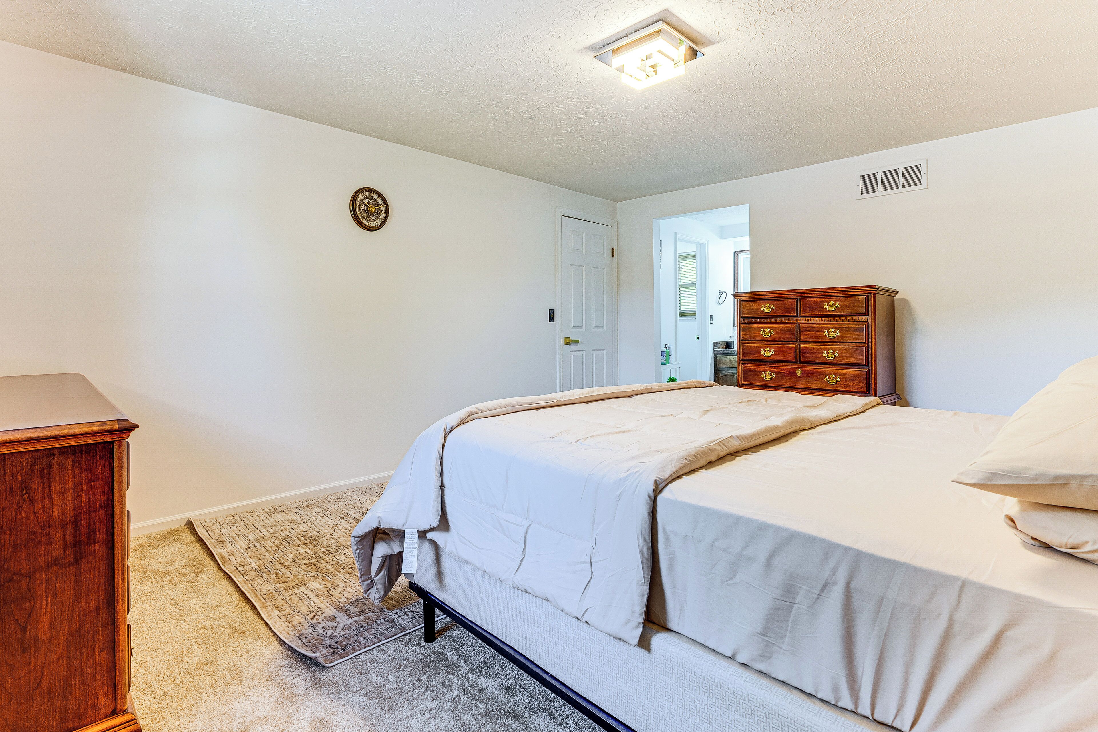 A bedroom with a bed, a wooden dresser, and a carpeted floor.