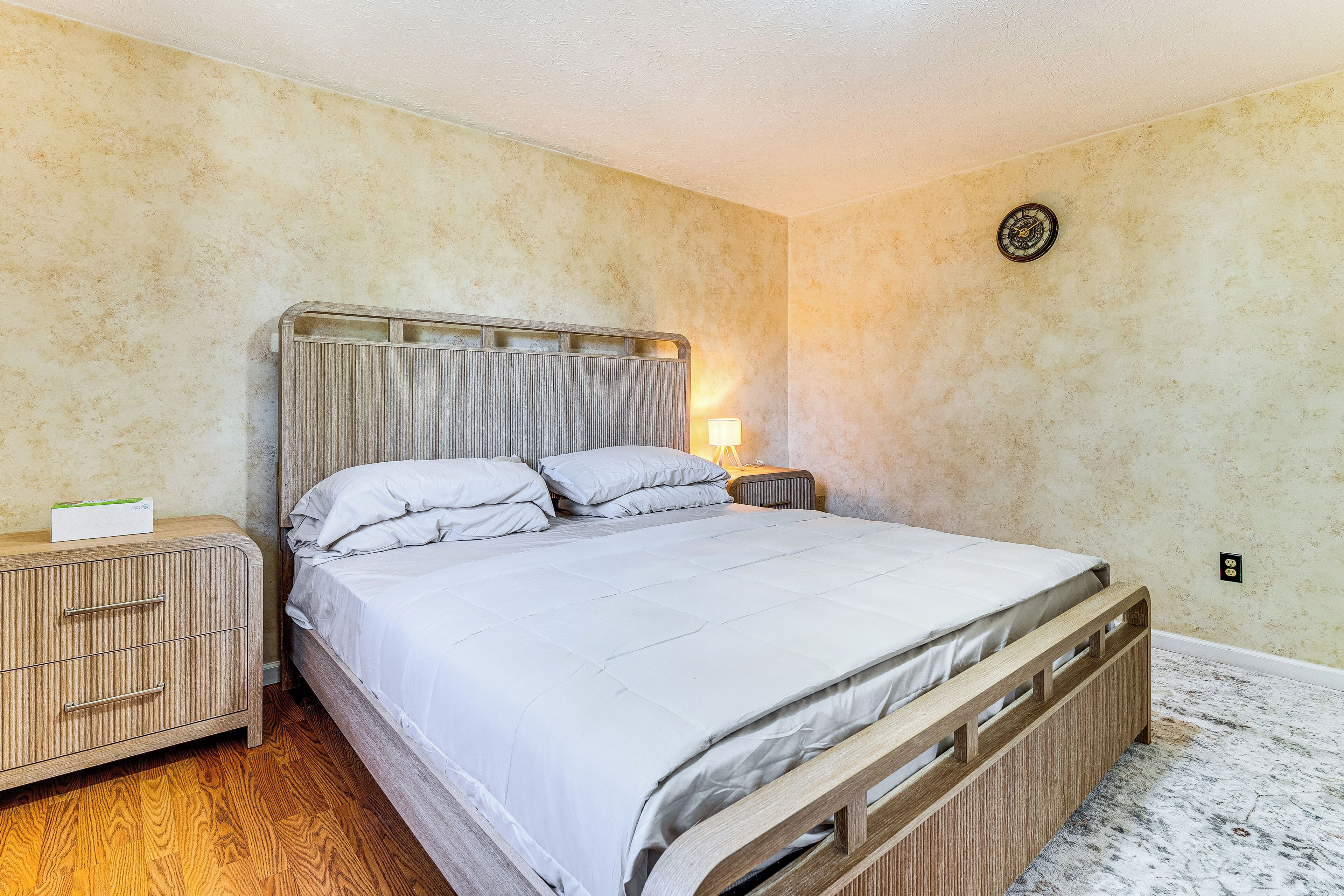 Un dormitorio con cama, mesita de noche de madera y una lámpara fijada a la pared.