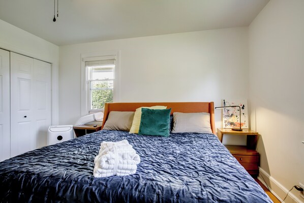 A bedroom with a large bed, a bedside table with a lamp, a window, and a door. - Marinafront Cottage Sunrise, Fire Pit, Fireworks (Cambridge)