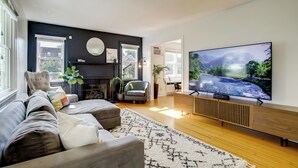 A modern living room with a large flat-screen TV, a fireplace, a sofa, and a large window. - Marinafront Cottage Sunrise, Fire Pit, Fireworks (Cambridge)