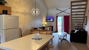 A compact kitchen with a central island, a dining area with a TV, and a living space with a sofa and a staircase. - Ski in/out 2b2b at Hunter! (Lanesville)