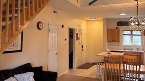 A spacious living area with a wooden staircase, a dining table with chairs, and a kitchen area visible through an open door. - Ski in/out 2b2b at Hunter! (Lanesville)
