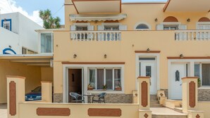 A two-story building with a balcony, a carport, and a small outdoor seating area.