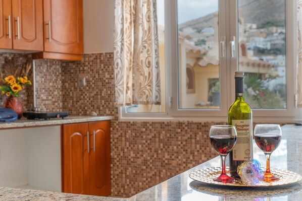 Una cocina con una botella de vino y copas sobre una bandeja, una ventana con vistas a edificios y armarios de madera.