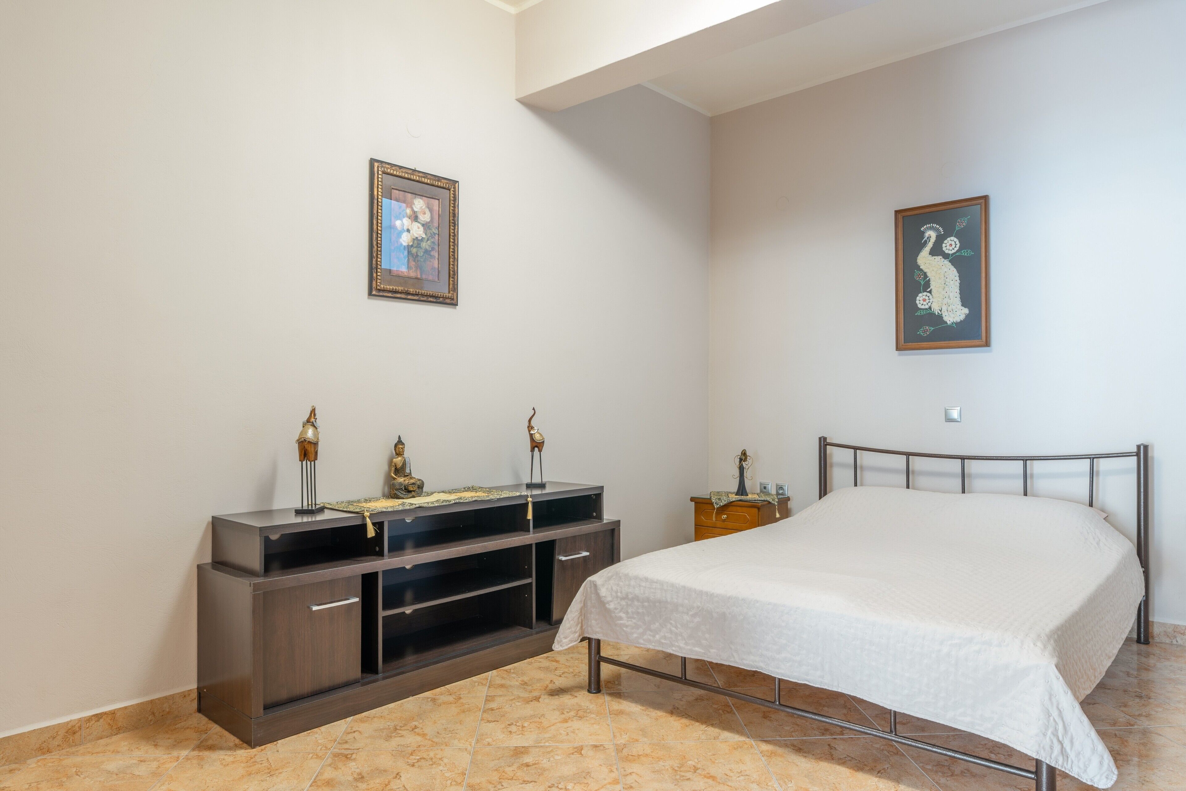 A bedroom with a bed, a dresser, a nightstand, and two wall-mounted pictures.