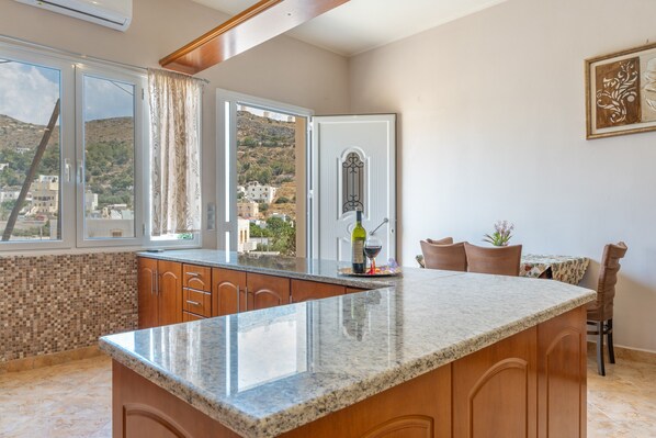 A kitchen with a large island, a dining area with chairs, and a view of a hillside through a window.