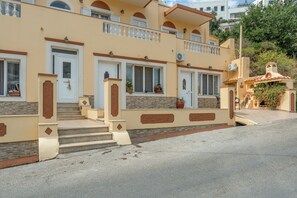 En toetages bygning med en beige facade, flere balkoner og en mindre tilbygning med et tag af fliser.
