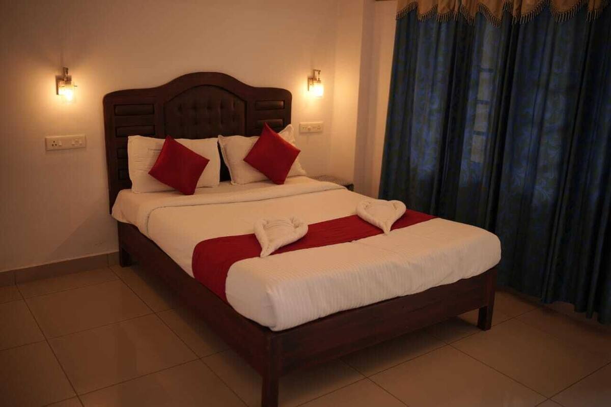 A neatly made bed with white and red bedding, two wall-mounted lights, and a dark curtain.