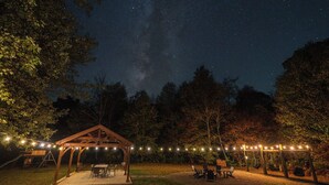 An outdoor patio area with a wooden pergola, string lights, and seating arrangements. - Aviation Cabin | Hot Tub • Fire Pit • River Access (Roulette)
