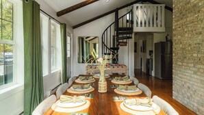 A dining area with a wooden table set for six, a staircase, and a brick wall. - Aviation Cabin | Hot Tub • Fire Pit • River Access (Roulette)