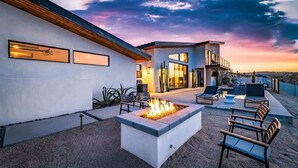 A modern outdoor patio with a fire pit, seating, and a view of a contemporary house. - The Mesa Horizon House By Homestead Modern (Yucca Valley)