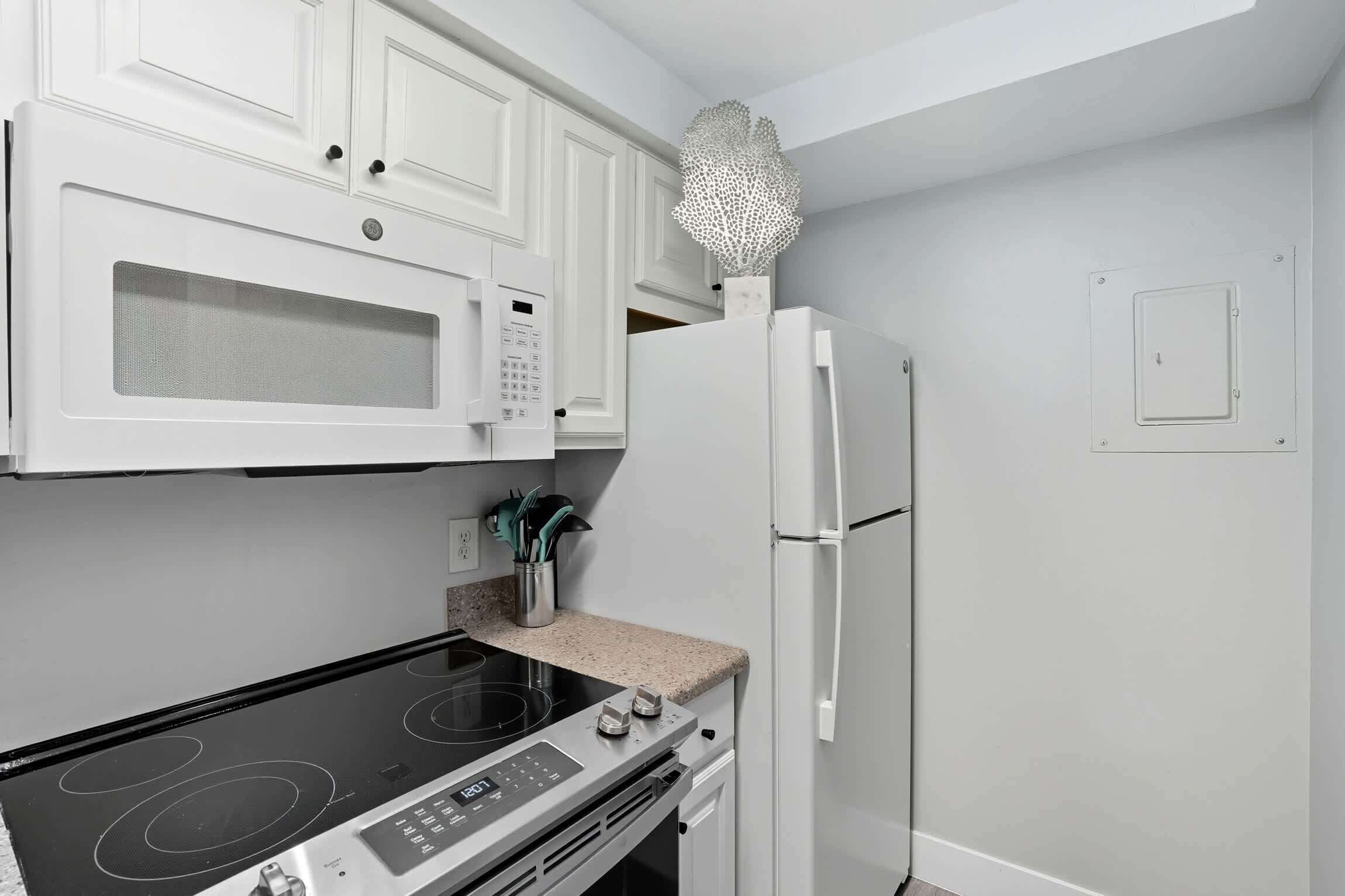 Een keuken met witte kastjes, een magnetron, een koelkast, een fornuis en een klein decoratief object aan de muur.