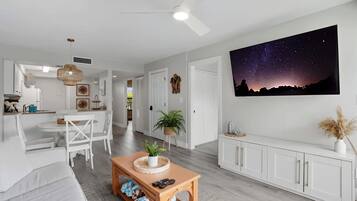 A modern living room with a white sofa, a wooden coffee table, and a dining area with white chairs.