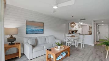 A modern living room with a sofa, coffee table, and a painting of a beach scene.