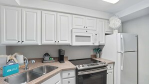 A modern kitchen with white cabinets, a stainless steel sink, a built-in microwave, a stove, and a refrigerator. - I-252 Updated With Views, Pool, & Near Beach! (Naples)