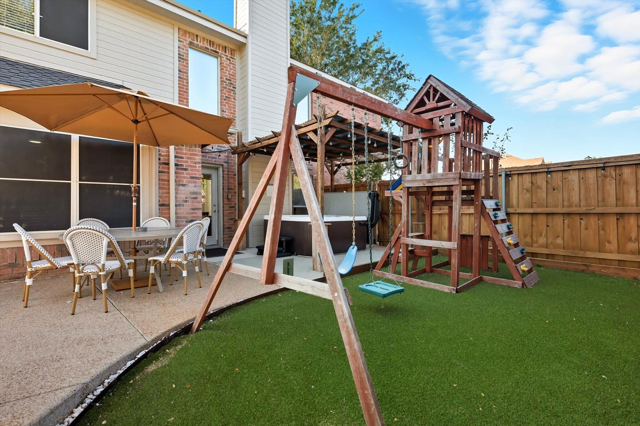 Ein Garten mit einer hölzernen Spielanlage, einem Patio-Tisch mit Stühlen und einer überdachten Sitzgruppe.