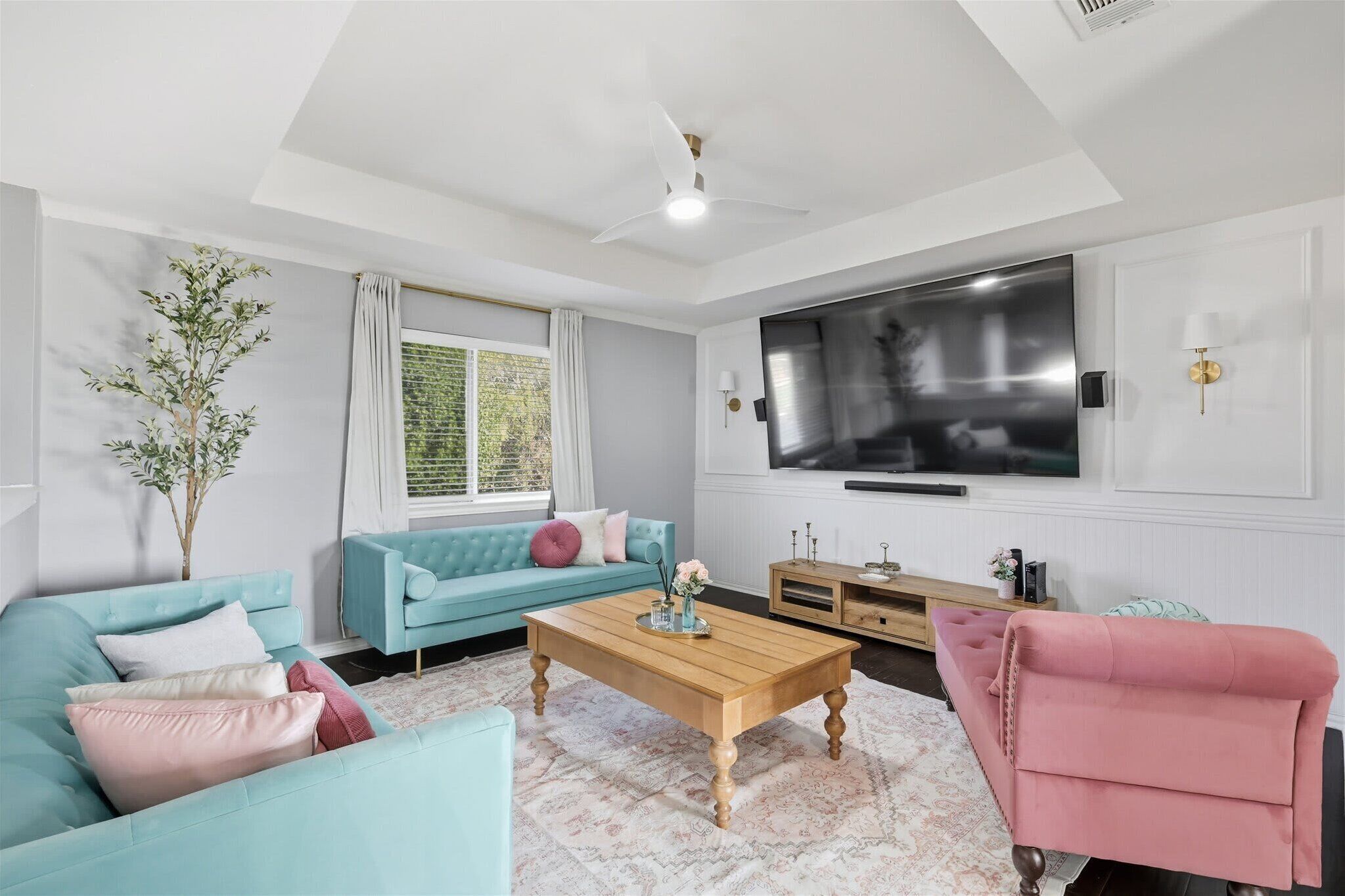 A living room with a blue sofa, a pink armchair, a wooden coffee table, and a large flat-screen TV mounted on the wall.