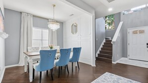 A dining area with a white table and blue chairs, a chandelier, and a staircase leading to a second floor. - French-Style 5-BD w/ Pool, Playground, Cinema (Lewisville)